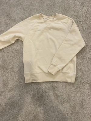 Beige sweatshirt med raglanärm - En stilren beige sweatshirt med raglanärmar och ribbade muddar vid hals, ärmslut och nederkant. Tröjan har en klassisk rund halsringning och är tillverkad i mjukt bomullsmaterial. Perfekt för en avslappnad och enkel look. Storlek 146/152