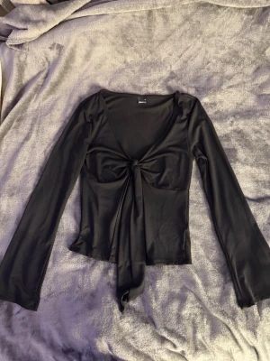 Svart långärmad topp Gina Tricot - Snygg svart långärmad topp från Gina Tricot med v-ringning och knyt framtill. Tillverkad i ett mjukt, stretchigt material som ger en slim passform. Perfekt att styla med jeans eller kjol för en trendig look.  Aldrig använd! 