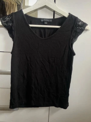 Svart topp med spetsärmar från XOXO Venus - Snygg svart topp från XOXO Venus med v-ringning och korta spetsärmar. Toppens material känns mjukt och stretchigt, perfekt för en trendig look. Spetsdetaljerna på ärmarna ger en extra touch och toppen har en slim passform.