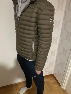 Olivgrön dunjacka från Colmar - Snygg olivgrön dunjacka från Colmar med quiltad design och två dragkedjeförsedda fickor. Jackan har hög krage och en diskret logga på ärmen. Perfekt för kalla vårdagar och lätt att matcha med olika outfits.