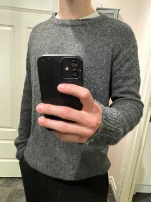 Mörkgrå stickad tröja  - Mysig mörkgrå stickad tröja med rund halsringning och långa ärmar. Tröjan har en enkel, klassisk design och är tillverkad i ett mjukt, grovt stickat material som passar perfekt för kyligare dagar.