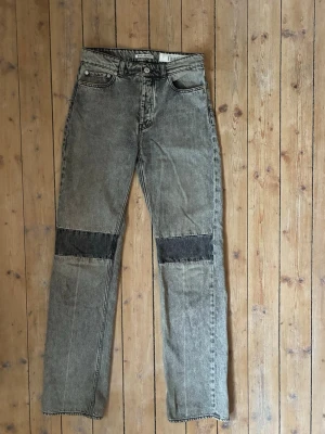 Grå patchwork jeans med raka ben - Unika grå jeans med raka ben och coola svarta patchwork-detaljer över knäna. Klassisk femficksmodell med kontrastsömmar och hög midja. Jeansen har en vintagekänsla och är tillverkade i kraftigt denimtyg, perfekta för en trendig streetwear-look.