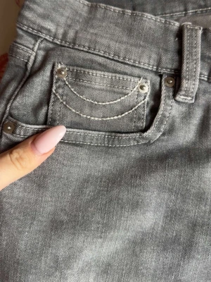 Grå jeans med kontrastsömmar - Säljer ett par grå jeans med vita kontrastsömmar och snygga detaljer på fickorna. Jeansen har klassisk femficksmodell och bälteshällor. Materialet är denim i bomull och passformen är rak. Perfekta för en trendig och avslappnad look. Nypris 600