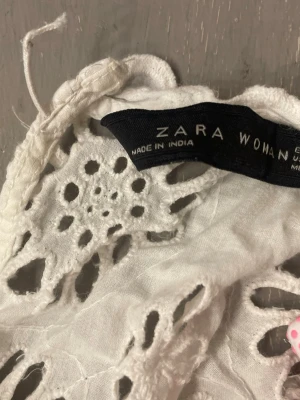Vit broderad blus från Zara Woman - Söt vit blus från Zara Woman med broderade blommönster och hålbroderier. Blusen har långa ärmar med elastiska muddar och volangdetaljer vid axlar och ärmslut. Tillverkad i ett lätt och luftigt material, perfekt för en trendig och romantisk look.
