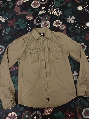 Overshirt - En grön-grå overshirt från märket Brandit storlek S. Gjord för att efterlikna en mer vintage-vibe. Perfekt för våren. Superfint skick, skriv vid minda fråga eller fundering!