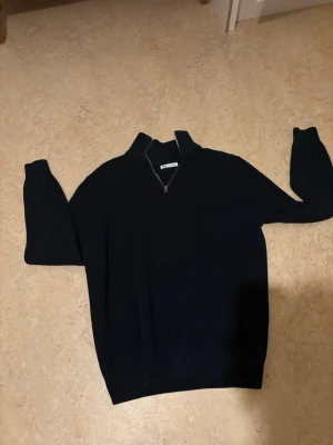 Mörkblå ribbstickad tröja med halvzip - Säljer en mörkblå ribbstickad tröja från med halvzip och hög krage. Tröjan har lång ärm och är tillverkad i ett mjukt material som ger en snygg passform. Perfekt för dig som gillar stilrena plagg med lite edge. Priset kan diskuteras!