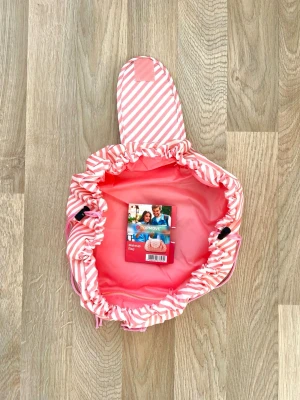 Make-up Pouch med dragsnöre - Den här praktiska sminkväskan i randig rosa från Topmove expanderas helt på några sekunder så att du ser allt innehåll på en gång. Dragsnöret gör att du snabbt stänger väskan och tar med dig allt du behöver. Den öppna formen ger dig full kontroll över innehållet och minskar risken att något göms i botten. Tillverkad i lätt syntetmaterial. Fick den i present. Aldrig använd, helt ny. 