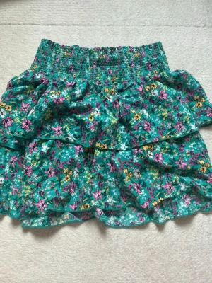 Grön blommig volangkjol - Supersöt grön kjol med blommigt mönster i rosa, gult och vitt. Kjolen är luftig och gjord i ett lätt bomullstyg. Perfekt för dig som gillar färg och mönster! Superfin till sommaren!🩷🩷