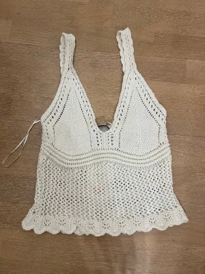 Vit stickad linnetopp från Zara - Supersöt vit stickad linnetopp från Zara med breda axelband och v-ringning. Toppen har virkad känsla, vågig kant nertill och är perfekt för varma dagar. Snygg att styla med jeans eller kjol för en chill look.