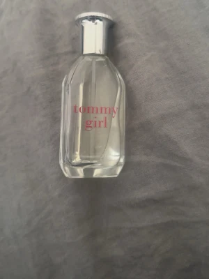 Tommy Girl parfym från Tommy Hilfiger - Fräsch parfym från Tommy Hilfiger, Tommy Girl. Flaskan är genomskinlig med silverfärgad kork och röd text. Klassisk och stilren design som passar perfekt i väskan eller på sminkbordet. Doften är lätt och ungdomlig. Hälften är kvar ungefär.