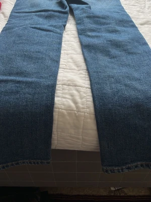 Blå raka jeans med kontrastsömmar - Säljer ett par klassiska blå jeans med rak passform och tydliga kontrastsömmar längs benen. Jeansen har en tidlös look och är tillverkade i denim. Perfekta för dig som gillar enkel och clean stil.