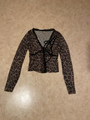 Leopardmönstrad mesh bolerotopp - Trendig bolerotopp i mesh med leopardmönster och långa ärmar. Toppen har snygga svarta snörningsdetaljer framtill och är croppad i modellen. Perfekt för att lyfta vilken outfit som helst.