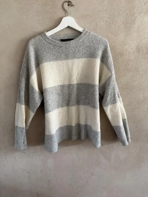 Grå vit randig stickad tröja från Vero Moda - Fin stickad tröja från Vero Moda, bra skick, knappt använd, passar till allt!