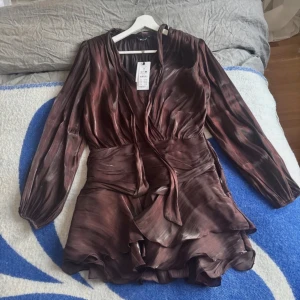 Brun klänning med volang - Brun miniklänning från Ginatricot, helt oanvänd endast testad. Nypris 599, slutsåld. 