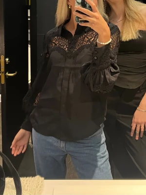 Svart spetsblus från Copenhagen Muse - Hej🩷Säljer en snygg svart blus från Copenhagen Muse med genombrutna spetsdetaljer över axlar och ärmar. Blusen har krage, knäppning framtill och vida långärmade ärmar med vackra spetsmönster. Perfekt för dig som vill ha en unik och trendig look.              Mycket bra skick! 