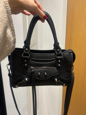 Svart handväska  - Snygg svart handväska  med silverfärgade metalldetaljer. I helt ok skick, endast slitage på insidan av handtagen men inget man tänker på annars bra. Får plats me mycket! 