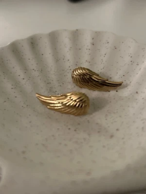 Edblad vinge örhängen  - Säljer ett par snygga örhängen i guldfärgad metall formade som vingar. De har en detaljerad, räfflad yta som ger en cool och unik look. Perfekta för dig som vill ha något lite extra till din stil. Örhängena är i rostfritt stål med guldplätering💞