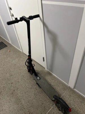 Svart elsparkcykel E-Wheels - Säljer en svart elsparkcykel från E-Wheels med bred fotplatta och robust ram. Utrustad med handtag i gummi, stora hjul och tydlig display på styret. Perfekt för att ta sig runt i stan på ett smidigt sätt.