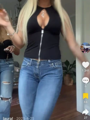 Svart croppad topp med dragkedja - Snygg svart croppad topp med dragkedja framtill och en djup v-ringning. Toppen är ärmlös och har en tajt passform som framhäver figuren. Perfekt för dig som vill ha en trendig och edgy look.