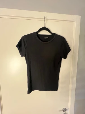 Svart tajt t-shirt  - En tajt svart t-shirt med rund hals och korta ärmar. Storlek M från Gina. Passar till det mesta. Skriv om du undrar något💕