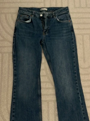 Blå bootcut jeans med vintagekänsla - Säljer ett par klassiska blå bootcut jeans i denim med lätt slitna detaljer och raka ben. Perfekta för en avslappnad och trendig look.