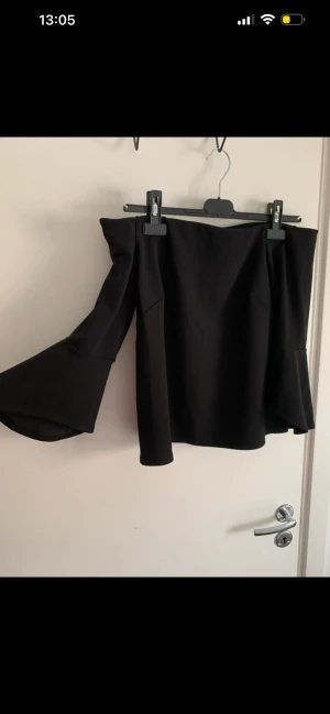 Svart offshoulder topp från H&M - Trendig svart offshoulder topp från H&M med vida ärmar och rak passform. Toppen är axelbandslös och har en stilren look som passar perfekt till många outfits. Tillverkad i mjukt syntetmaterial för en bekväm känsla.