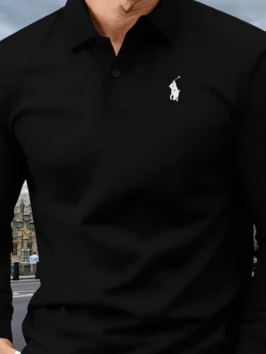 Svart långärmad pikétröja från Polo Ralph Lauren - Svart långärmad skjorta från Polo Ralph Lauren med klassisk krage och knappslå framtill. Ikonisk vit broderad logga på bröstet. Skjortan är stilren och har en slim passform, troligtvis i bomull.