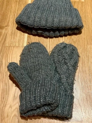 Grå stickad mössa med pälsboll - Säljer en grå stickad mössa med ribbad kant och en fluffig pälsboll på toppen. Mössan är gjord i mjukt garn och har en klassisk form. Perfekt för kalla dagar och matchar enkelt med olika stilar.