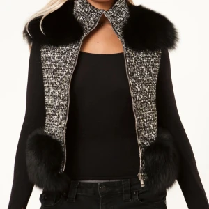 Svart och grå pälsväst med dragkedja - Trendig pälsväst från ALESSA svart och grått med fluffiga svarta pälskanter vid axlar och nederkant. Stängs med dragkedja framtill. 