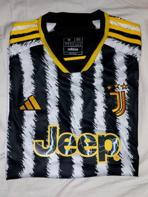 Juventus matchtröja Adidas svartvit - Juventus tröja från Adidas i svartvitt zebramönster med gula detaljer. Tröjan har klubbmärke, Adidas-logga och Jeep som sponsor framtill. Tillverkad i lätt och ventilerande polyester, perfekt för fotboll eller träning.