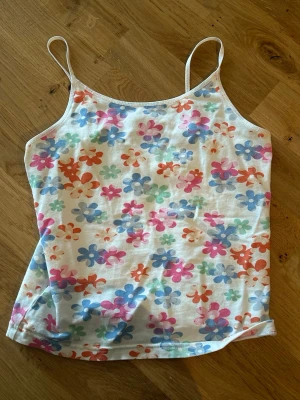 Blommig linnetopp med smala band - Säljer en söt linnetopp med smala axelband och blommigt mönster i rosa, blått, orange och grönt på vit botten. Storlek xs/s