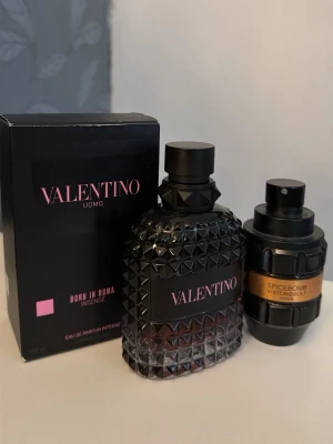 Valentino Uomo Born In Roma & Spicebomb - Två exklusiva parfymer: Valentino Uomo Born In Roma Intense i en svart, mönstrad glasflaska med rosa detaljer och tillhörande kartong, samt Viktor & Rolf Spicebomb i en robust, svart flaska med guldetikett. Båda dofterna är Eau de Parfum och har lyxig design.