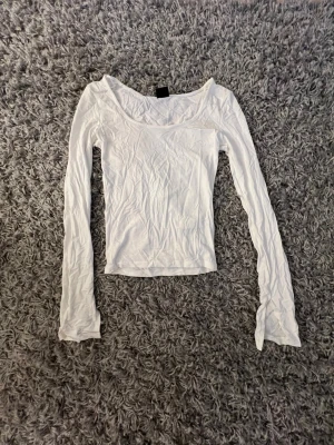 Vit långärmad topp med bred ringning - En enkel och stilren vit långärmad topp med bred ringning. Oanvänd från Gina i storlek XS. Toppen är figurnära och tillverkad i mjukt bomullsmaterial, perfekt att matcha med jeans eller kjol för en clean look. Skriv om du undrar nått💕