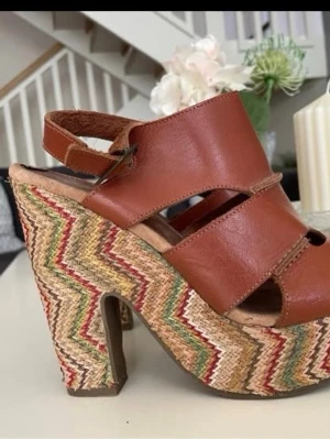 Nilsons högklackade sandaler strl 39 – färgglad kilklack - Snygga högklackade sandaler från Nilsons i storlek 39. Bruna remmar med färgglad kilklack som gör dem riktigt unika. Endast använda ett par gånger. Lite slitage på innersulan finns, se bilder, men annars i mycket fint skick. Kan upplevas som något små i storleken.