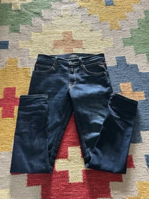 Mörkblå slim jeans från Replay - Säljer ett par mörkblå slim jeans från Replay med klassisk femficksdesign och kontrastsömmar. Jeansen har en smal passform och Replay-logga på bakfickan. Perfekta för en trendig och avslappnad look.