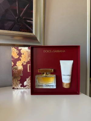 Dolce & Gabbana The One presentset - Lyxigt presentset från Dolce & Gabbana med parfymen The One och en matchande body lotion. Parfymflaskan är elegant i glas med guldigt lock och har en varm gul nyans. Setet levereras i en snygg röd ask med guldiga detaljer.