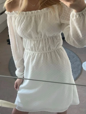 Vit offshoulder klänning - Superfin vit kortklänning med offshoulder och långa ärmar. Klänningen har små prickar i tyget och resår i midjan för en snygg passform. Perfekt nu till sommaren! Endast använd 2ggr. Slutsåld!! 💗💗