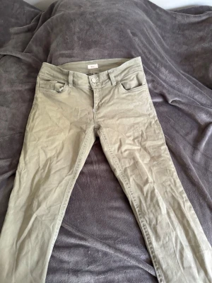 Gröna jeans från Nelly - Snygga gröna jeans från Nelly med smal passform och klassisk femficksdesign. Byxorna har dubbla knappar i midjan och bälteshällor. Perfekta för dig som vill ha en stilren och trendig look. Dom är lite sönder pågrund av att jag trampat på dom när jag har gått. Annars inget fel på dem.