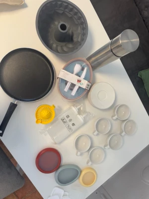 Stort kökspaket med formar och muggar - Säljer ett kökspaket med grå sockerkaksform i silikon, svart stekpanna, termos i rostfritt stål, citruspress, plastbestick, flera vita koppar med fat samt färgglada små skålar. Perfekt för dig som vill fylla på köket med praktiska grejer.
