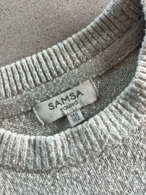 Randig stickad tröja från SAMSA Young - Säljer en beige stickad tröja från SAMSA Young med svarta horisontella ränder. Tröjan har rund halsringning, långa ärmar och ribbade muddar vid ärmslut och nederkant. Perfekt för dig som gillar enkel och stilren design.