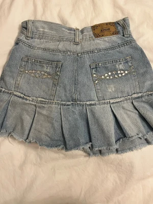 Ljusblå jeanskjol med volang - Superfin ljusblå vintage jeanskjol med volangkant. Kjolen har fickor både fram och bak, där bakfickorna är dekorerade med silvriga pärlor. Perfekt för dig som gillar en trendig och avslappnad stil. Midjemåttet på kjolen är ca 70 cm.                                              Säljer eftersom den inte passar mig.