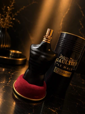 Jean Paul Gaultier Le Male Le Parfum - Jean Paul Gaultier Le Male Le Parfum i en svart, matt flaska formad som en manlig torso med gulddetaljer. Flaskan står på en rund, röd sammetsliknande bas och kommer med en svart metalltub med guldfärgad text. En ikonisk och lyxig parfymflaska.