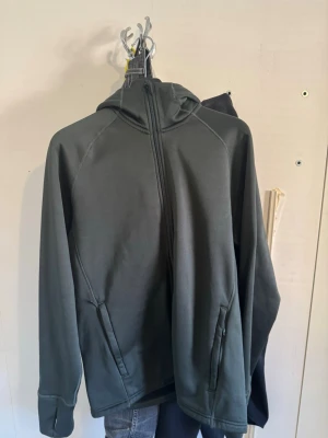 Mörkgrå hoodie från Everest - Snygg mörkgrå hoodie från Everest med dragkedja framtill och två fickor. Hoodien har huva och är tillverkad i ett mjukt, stretchigt material som känns skönt mot huden. Perfekt för dig som gillar en enkel och stilren look.