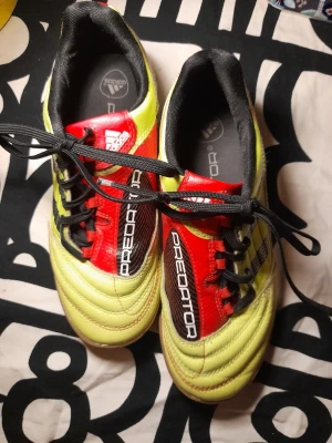 Adidas Predator gula fotbollsskor - Sällsynta Adidas Predator fotbollsskor i gult med röda och svarta detaljer. Skorna har klassisk låg profil, snörning och mönstrad sula för bra grepp på planen. Ovandelen är i syntetmaterial och designen har tydliga loggor och Predator-tryck.