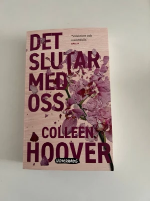 Det slutar med oss av Colleen Hoover - En gripande roman av Colleen Hoover med ett omslag i ljusrosa toner och blommotiv. Boken handlar om Lily som kämpar med kärlek, relationer och sitt förflutna. Perfekt för dig som gillar känslosamma och insiktsfulla berättelser. Första boken i serien. 