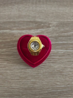 Guldfärgad ringklocka Quartz - Unik guldfärgad ringklocka med vit urtavla och tydliga svarta siffror. Klockan har en klassisk rund form och bärs som en ring. Perfekt accessoar för dig som vill sticka ut och kombinera smycke med funktion.