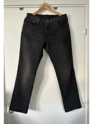 Levis - svarta raka jeans - storlek L / W30 L30 - Stilrena svarta Levi's 541 jeans i storlek W30 L30 med en klassisk design. Jeansen har en knappgylf och fem fickor, inklusive två bakfickor med Levi's signaturstickning och en liten röd flik på den högra bakfickan. Midjebandet har hällor för bälte. Stabil vävd denim i 70% bomull, 28% lyocell och 2% elastan, så bra material som andas och har lite stretch för bästa passform. Mycket gott skick!
