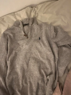 Grå halvzip-tröja från Polo Ralph Lauren - Snygg grå halvzip-tröja från Polo Ralph Lauren med klassisk broderad logga på bröstet. Tröjan har hög krage med dragkedja och ribbade muddar vid ärmslut och nederkant. Perfekt för lager-på-lager och chill stil.