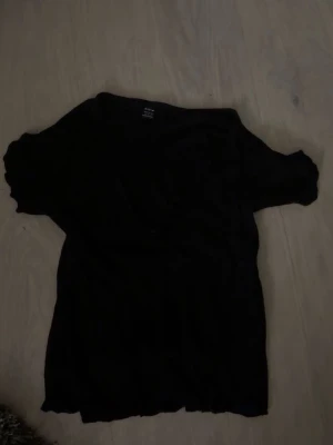 Svart omlottopp från Shein  - Svart omlottopp från Shein med korta ärmar och mjukt, lätt material. Toppen har en avslappnad passform och är perfekt att styla med jeans eller kjol. Enkel och stilren design som funkar till många olika looks.
