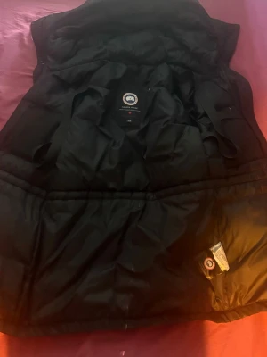 Svart dunväst från Canada Goose - Säljer en Canada Goose-jacka i storlek XS. Varm och skön medellång modell med huva och flera praktiska fickor.  Jackan är begagnad och har lite smuts/slitage på vissa ställen. Den är inte nytvättad, vilket återspeglas i priset. I övrigt är den i bra skick.  Pris: 2 000 kr Vid snabb affär kan priset diskuteras Storlek: XS                                                              Färg: Svart 📍 Finns i Stockholm  Skicka meddelande vid intresse eller om du vill ha fler bilder.